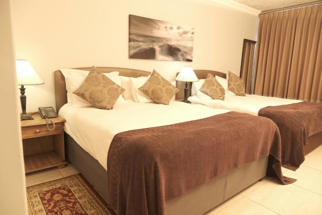 A double bed with a brown blanket, a bedside table with a lamp, a phone, and a wall-mounted picture.