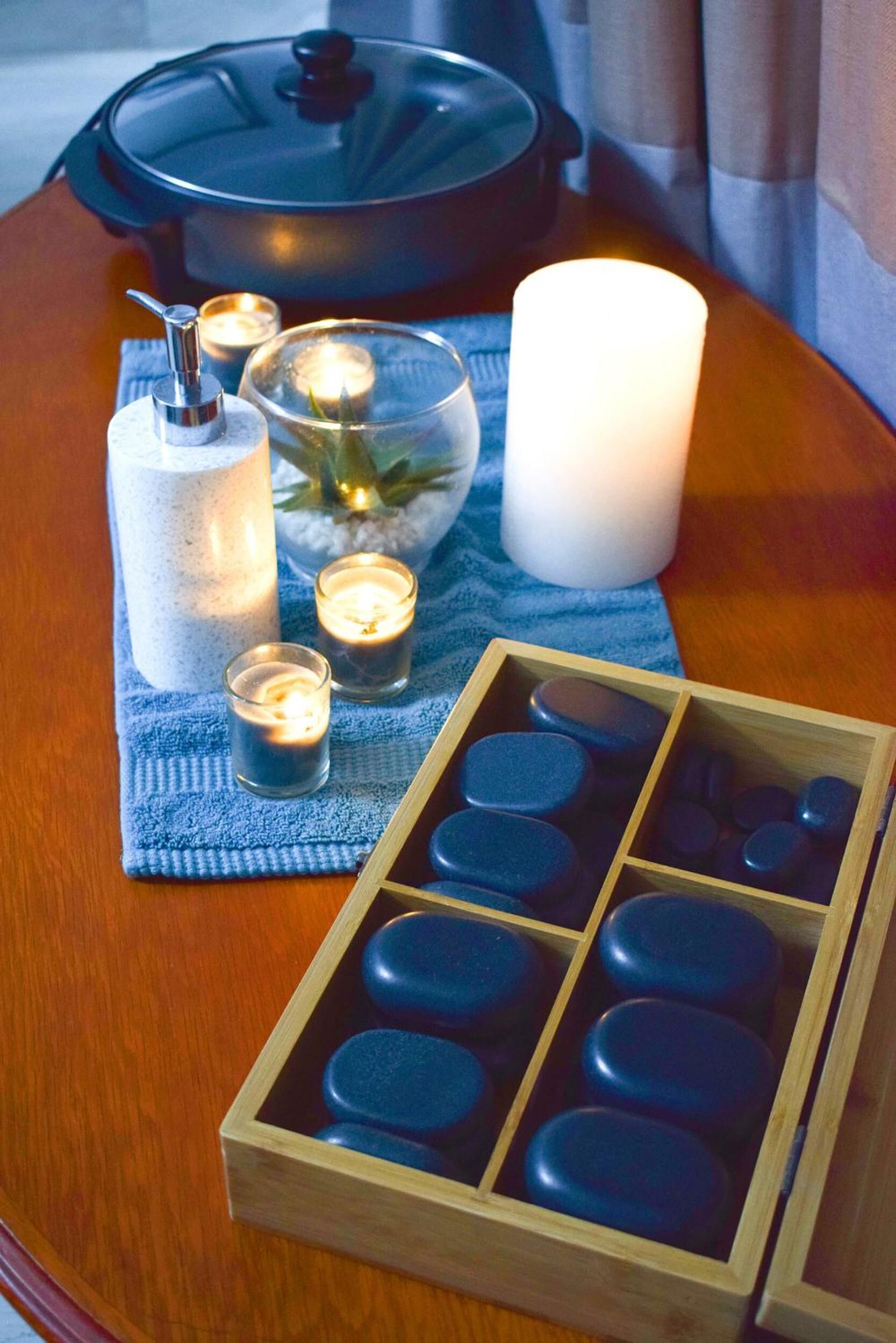 A wooden table with a candle holder, a candle, a glass of water, and a box of blue round objects.