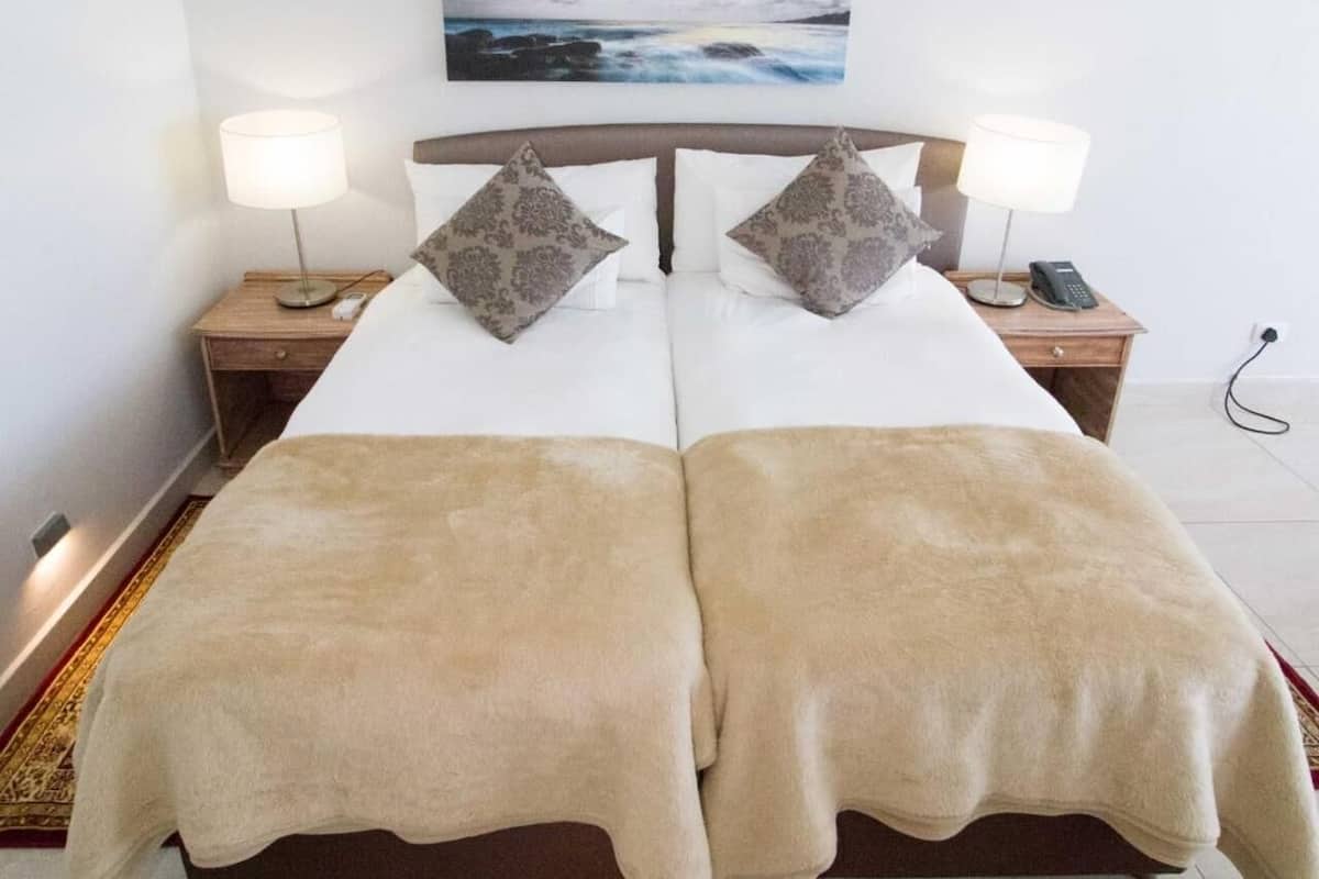 A double bed with two pillows, a bedside table with a lamp, and a painting above the bed.