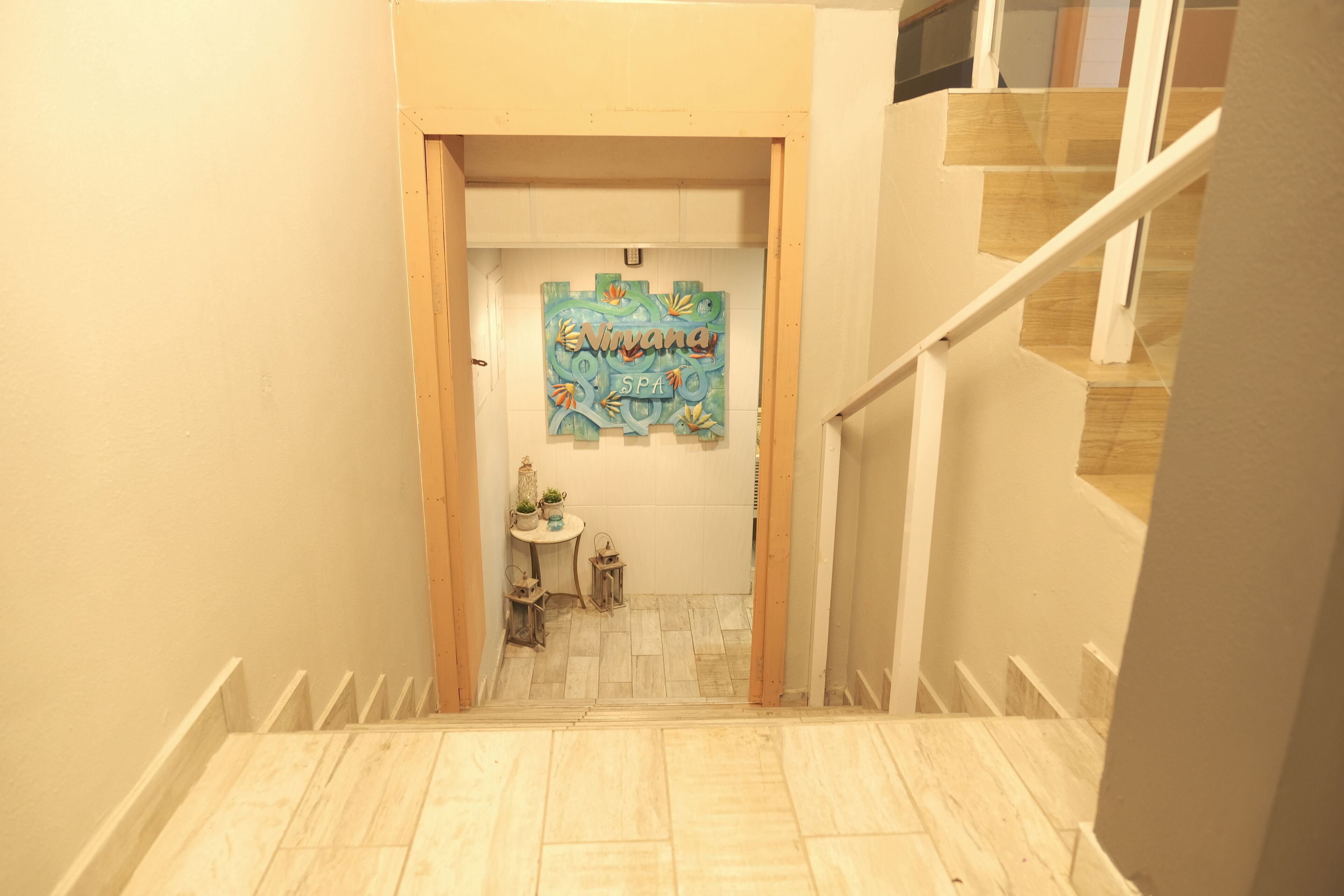 Eine Treppe führt zu einem Raum, an dessen Tür ein Schild mit 'Nirvana Spa' steht. Außerdem befindet sich ein kleiner Tisch mit einer Pflanze und ein Laternen auf dem Boden.