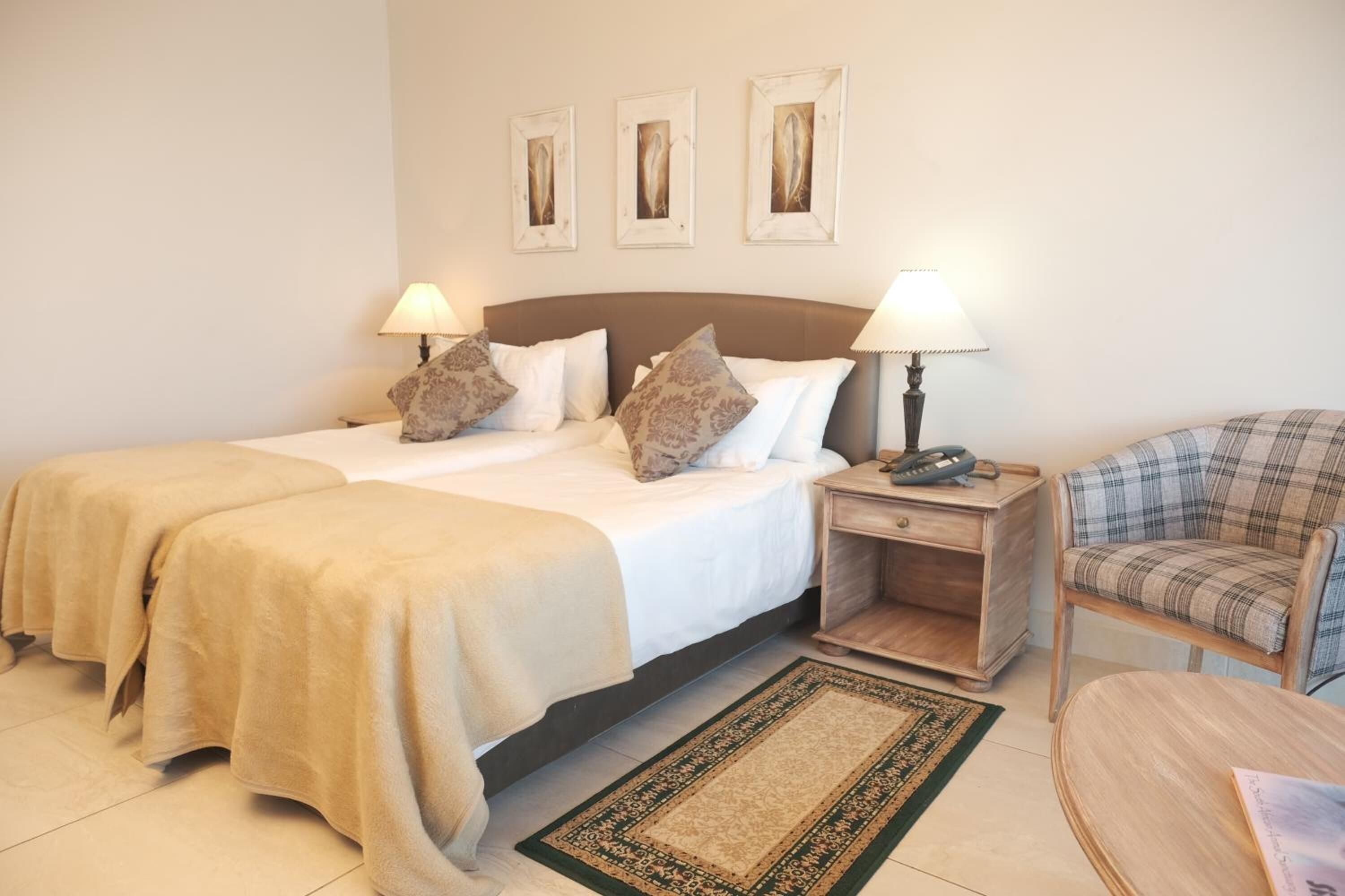 A hotel room with two beds, a nightstand, a chair, and a small table.