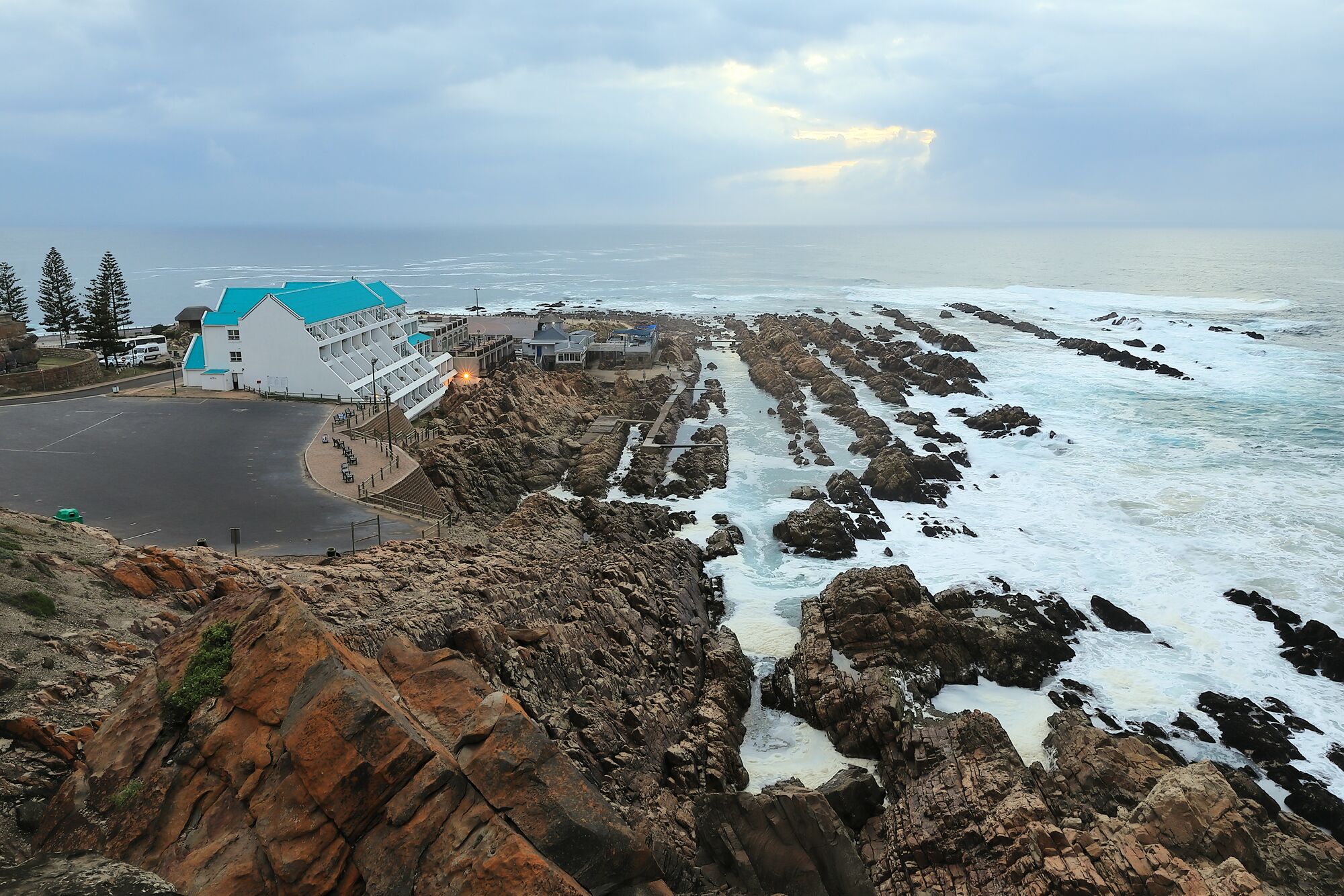 A coastal hotel with a white building and blue roof, rocky shoreline, and ocean view.