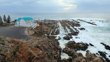 A coastal hotel with a white building and blue roof, rocky shoreline, and ocean view.