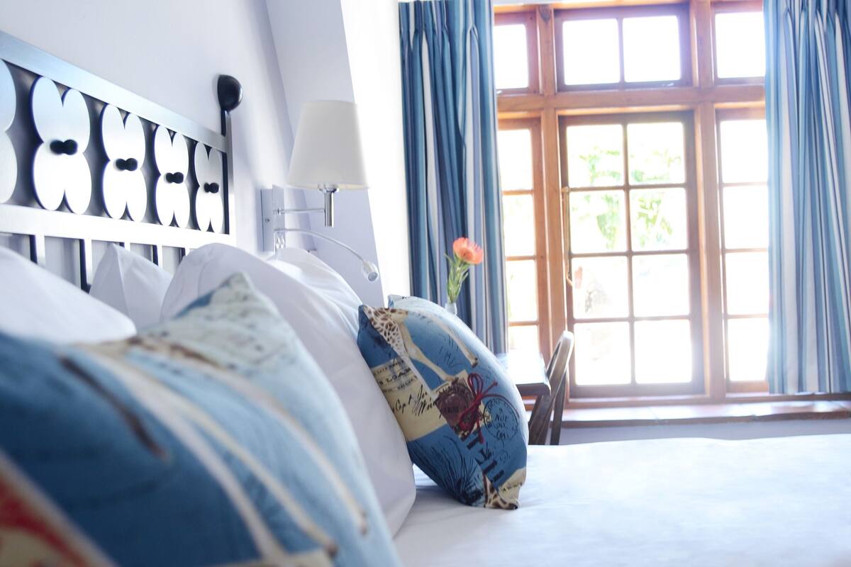 A hotel room with a bed, a nightstand, a lamp, and a window with curtains.