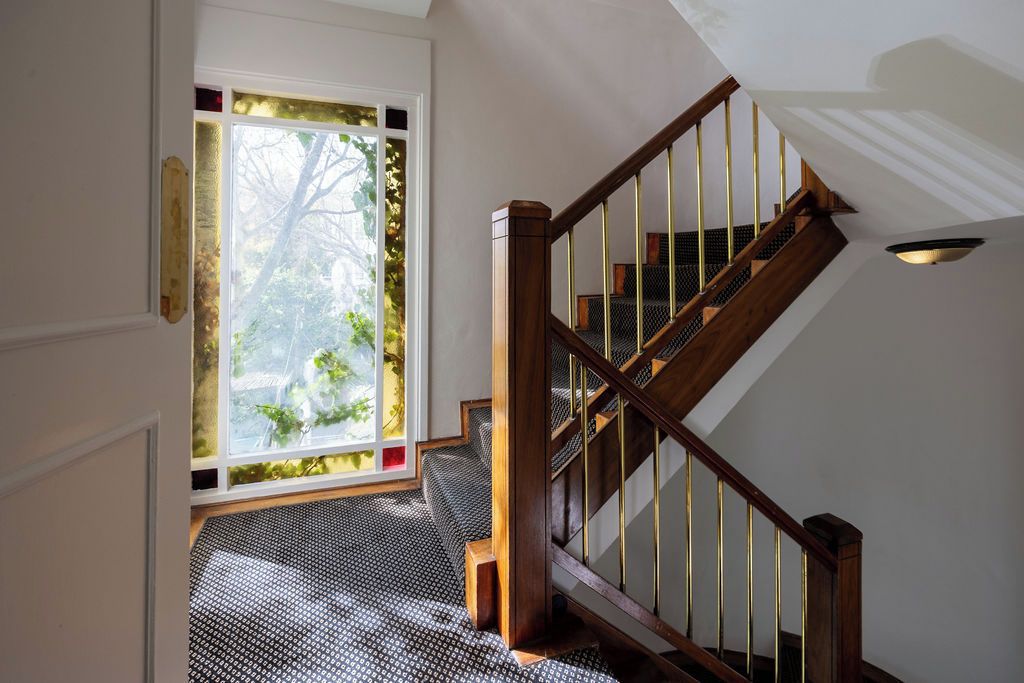 Una escalera con barandas de madera y un suelo estampado que lleva a una habitación con un gran ventanal.