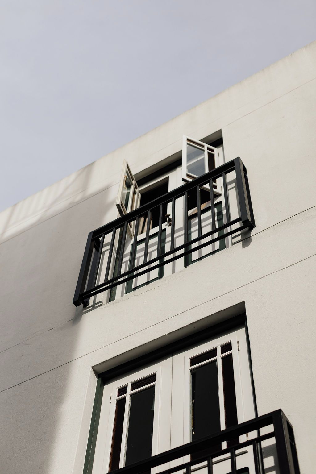 Un edificio con fachada blanca, marcos de ventana negros y un balcón con barandilla negra.