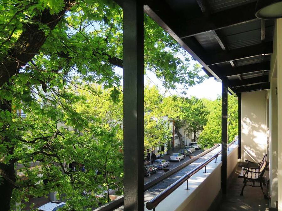 Un balcon fermé offrant une vue sur une rue bordée d’arbres.