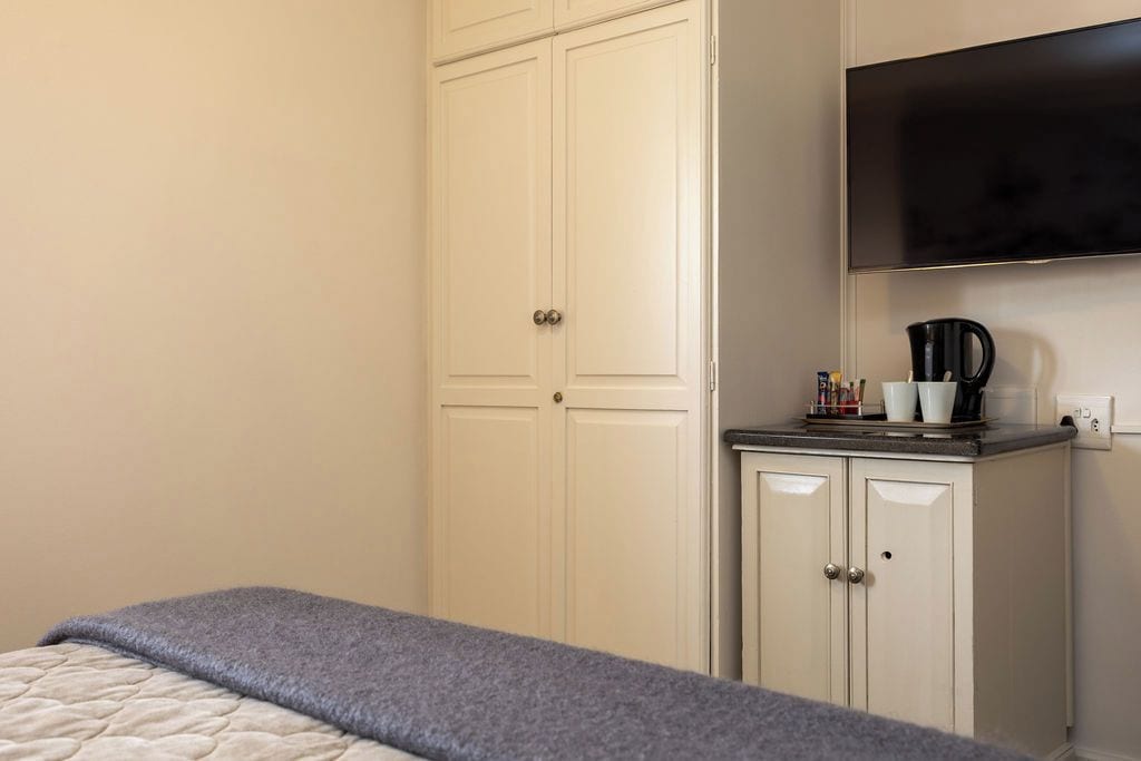Een slaapkamer met een bed, een kledingkast, een televisie en een koffiezetapparaat op een aanrecht.