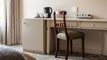 A compact kitchenette with a refrigerator, a coffee maker, and a power strip on the wall.