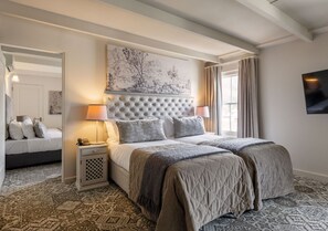 A bedroom with a tufted headboard, a bed with grey bedding, a bedside table with a lamp, and a patterned carpet. - The Stellenbosch Hotel (Stellenbosch)