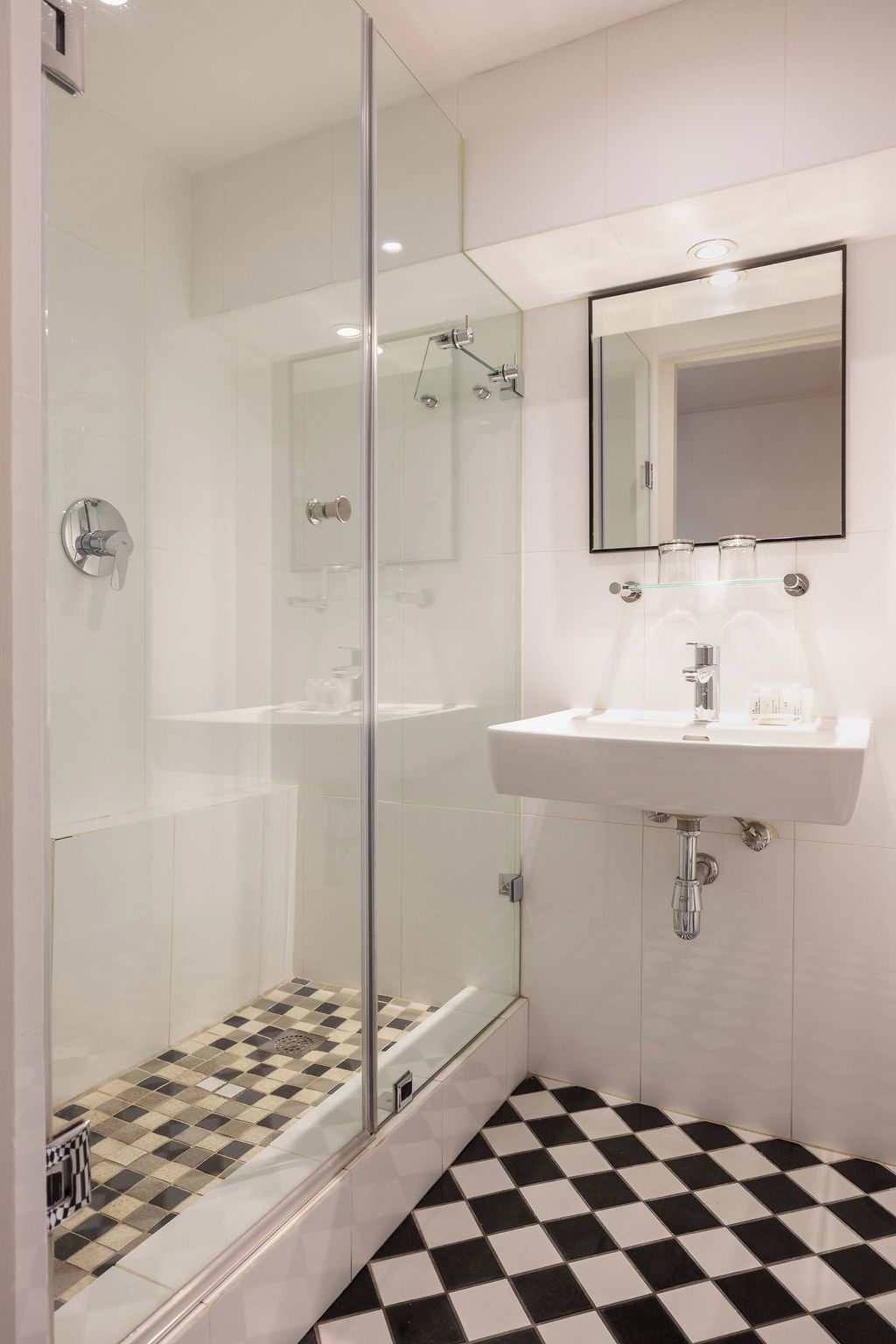 Un baño moderno con ducha de vidrio, un lavamanos blanco y piso a cuadros.