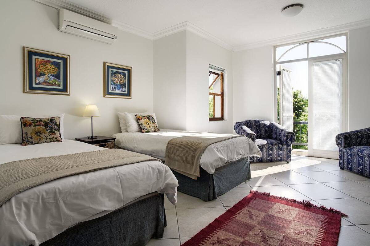 A hotel room with two beds, a sofa, a chair, and a large window with blinds.
