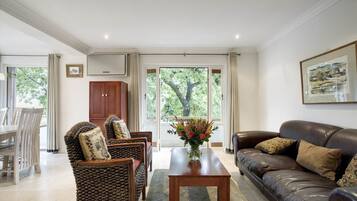 A spacious living room with a brown leather sofa, wicker chairs, a wooden coffee table, and a dining area with a white table and chairs.