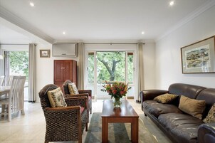 Amplia sala de estar con un sofá de cuero marrón, sillas de mimbre, una mesa de centro de madera y un comedor con mesa y sillas blancas.
