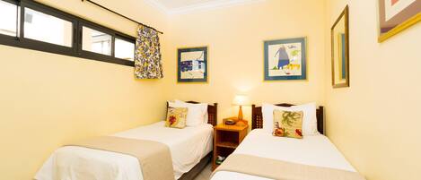 A hotel room with two single beds, a window with a curtain, and framed artwork on the walls.
