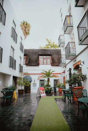 A courtyard with a thatched-roof building, green chairs, and potted plants. - The Stellenbosch Hotel (Stellenbosch)
