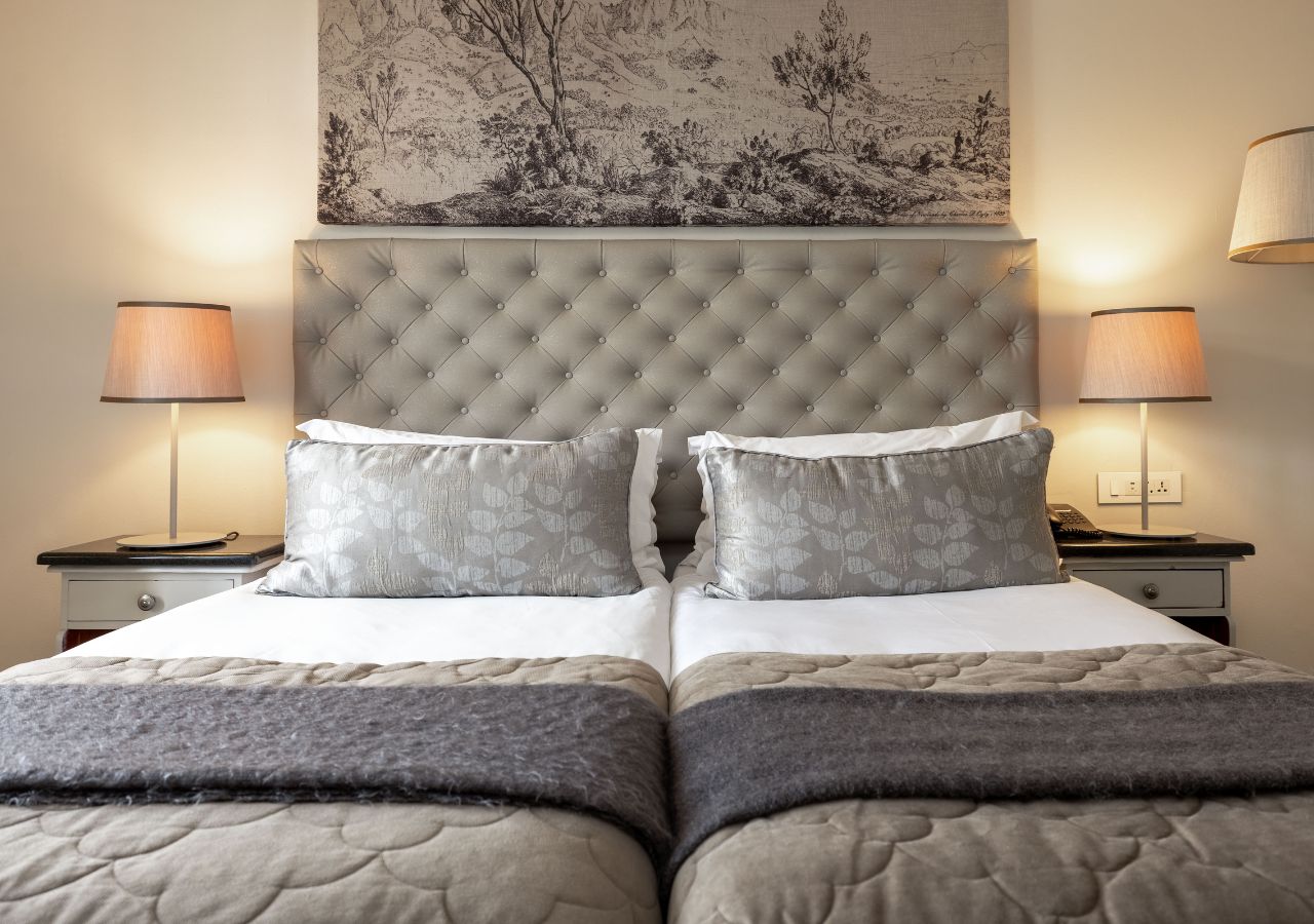 Una cama doble con cabecera capitonada, dos mesitas de noche con lámparas y una obra de arte colgada en la pared.