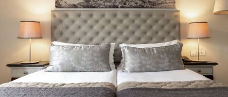 Una cama doble con cabecera capitonada, dos mesitas de noche con lámparas y una obra de arte colgada en la pared.