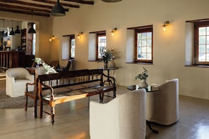 A spacious room with a wooden bench, two armchairs, a small table, and a bar area in the background. - The Stellenbosch Hotel (Stellenbosch)