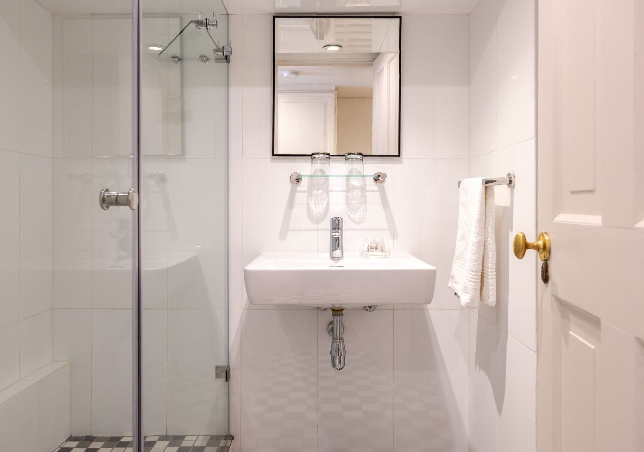 A bathroom with a glass shower enclosure, a white sink with a mirror above it, and a towel rack with a white towel.