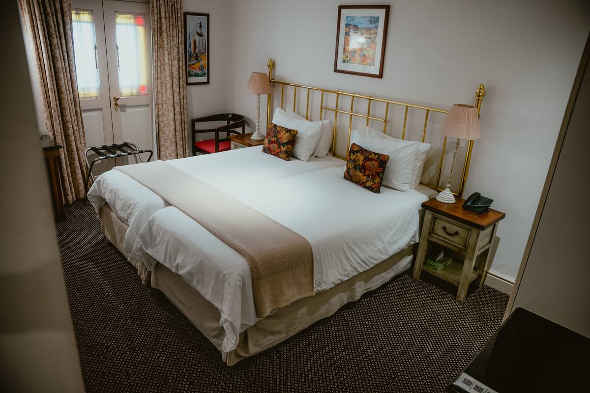 A neatly made bed with a gold headboard, a bedside table with a lamp, and a chair.