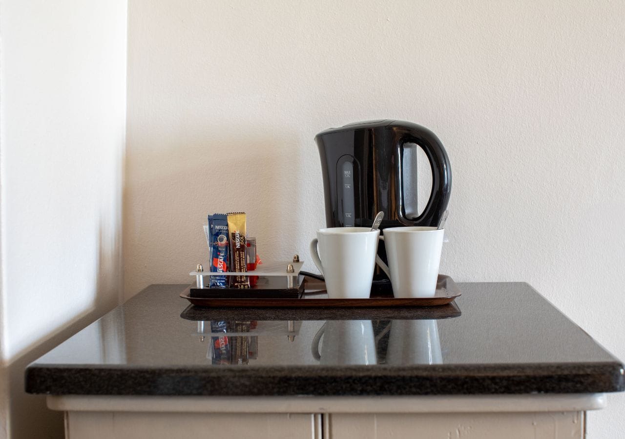 En köksbänk med en kaffebryggare, två vita koppar och ett bricka med kaffekapslar och en liten flaska.