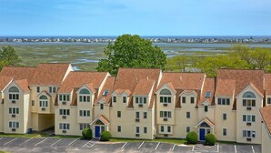 A row of beige multi-story buildings with brown roofs, arranged in a linear fashion with a parking lot in the foreground. - Village by the Sea (Wells)