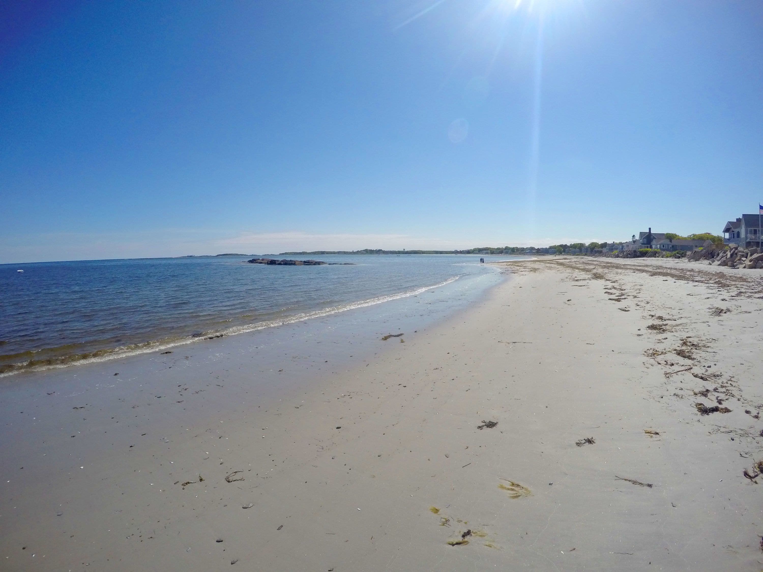 A beach with a clear sky, calm sea, and a few people walking.