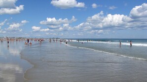 A beach with people swimming and walking along the shore. - Village by the Sea (Wells)