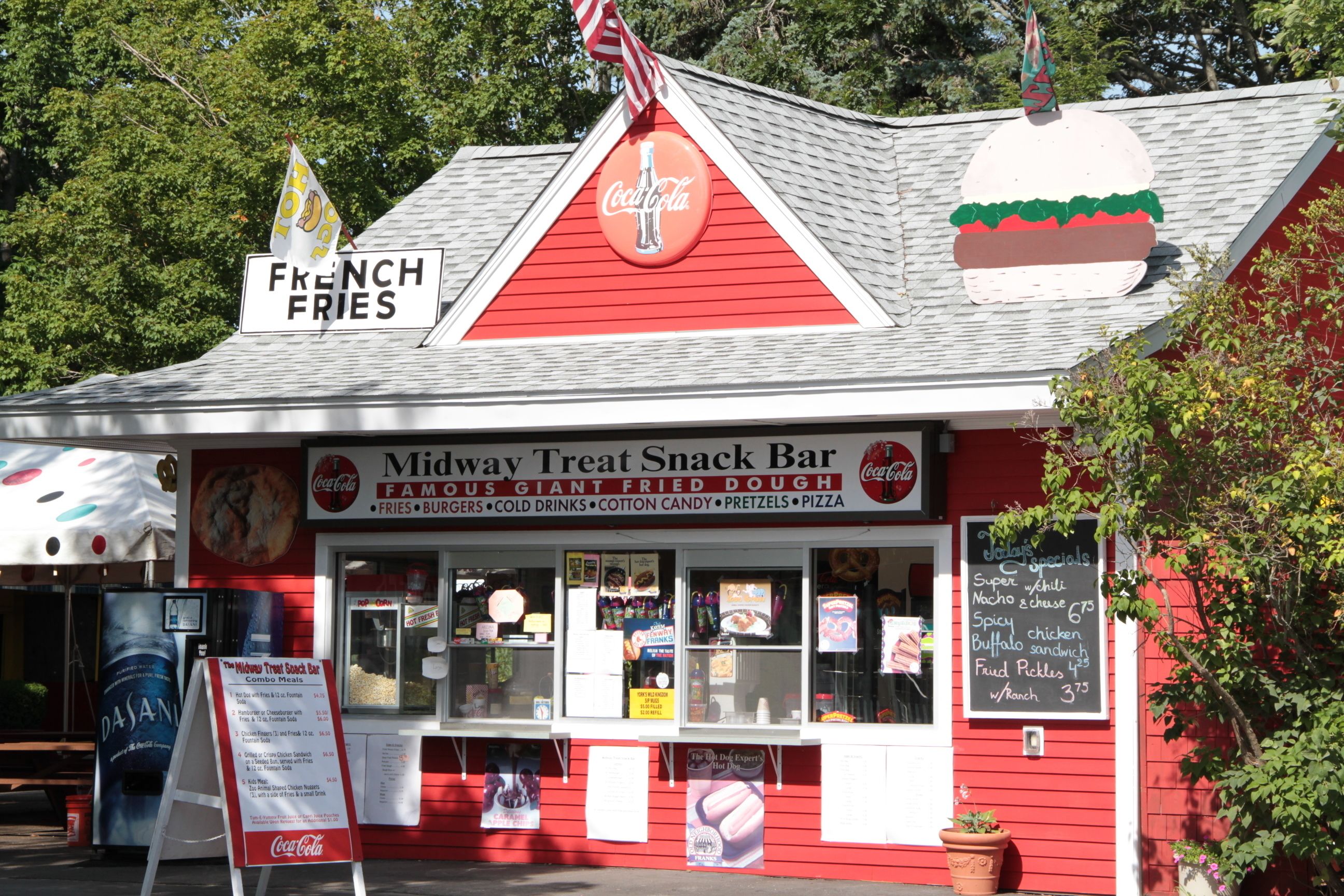 A red building with a sign for Midway Treat Snack Bar, featuring a Coca-Cola logo and a menu board.