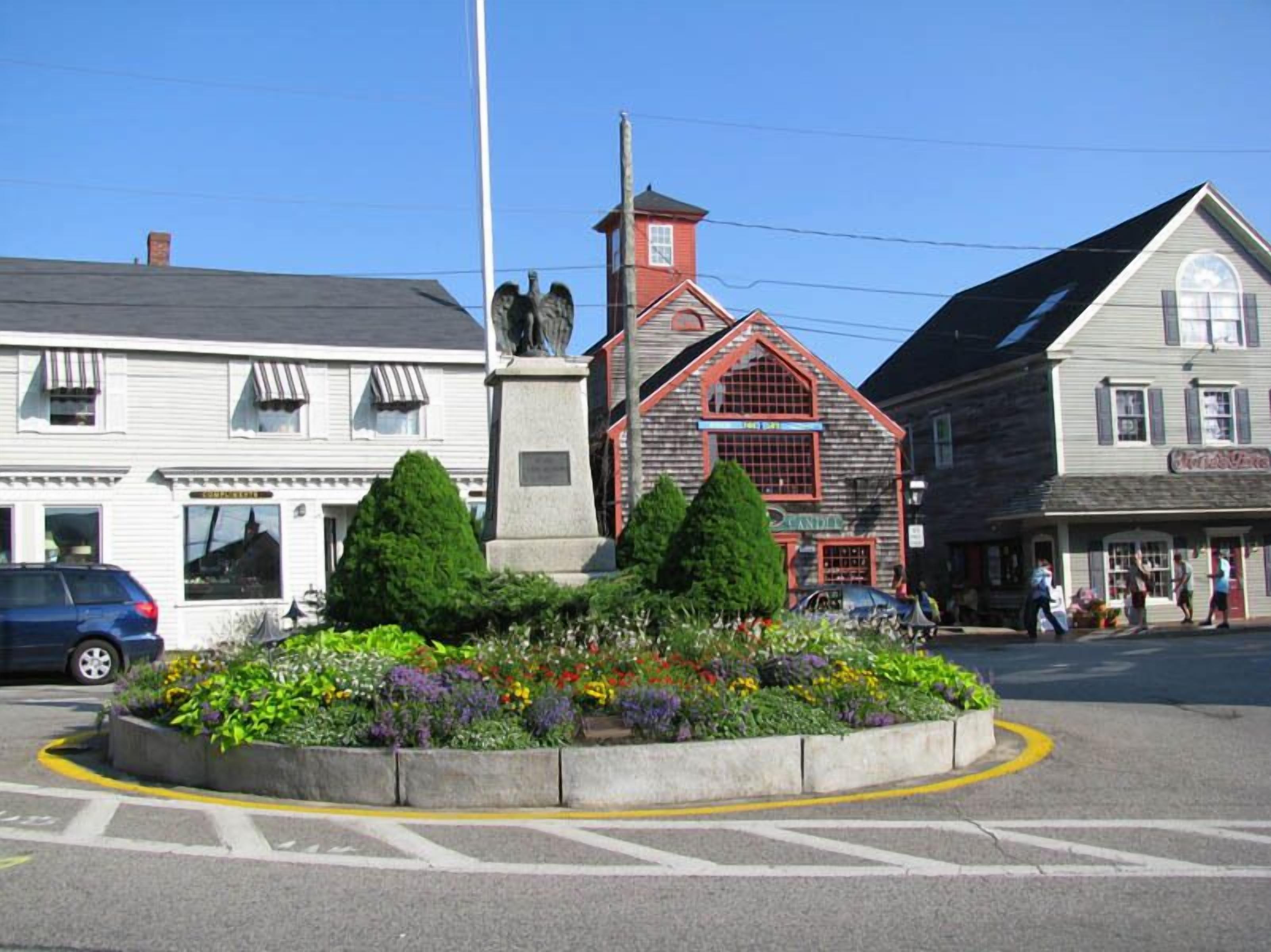 Una calle con un parterre, una estatua y edificios con escaparates.
