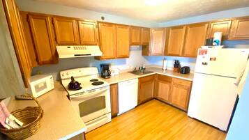 A compact kitchen with wooden cabinets, a white stove, a microwave, a dishwasher, and a refrigerator.