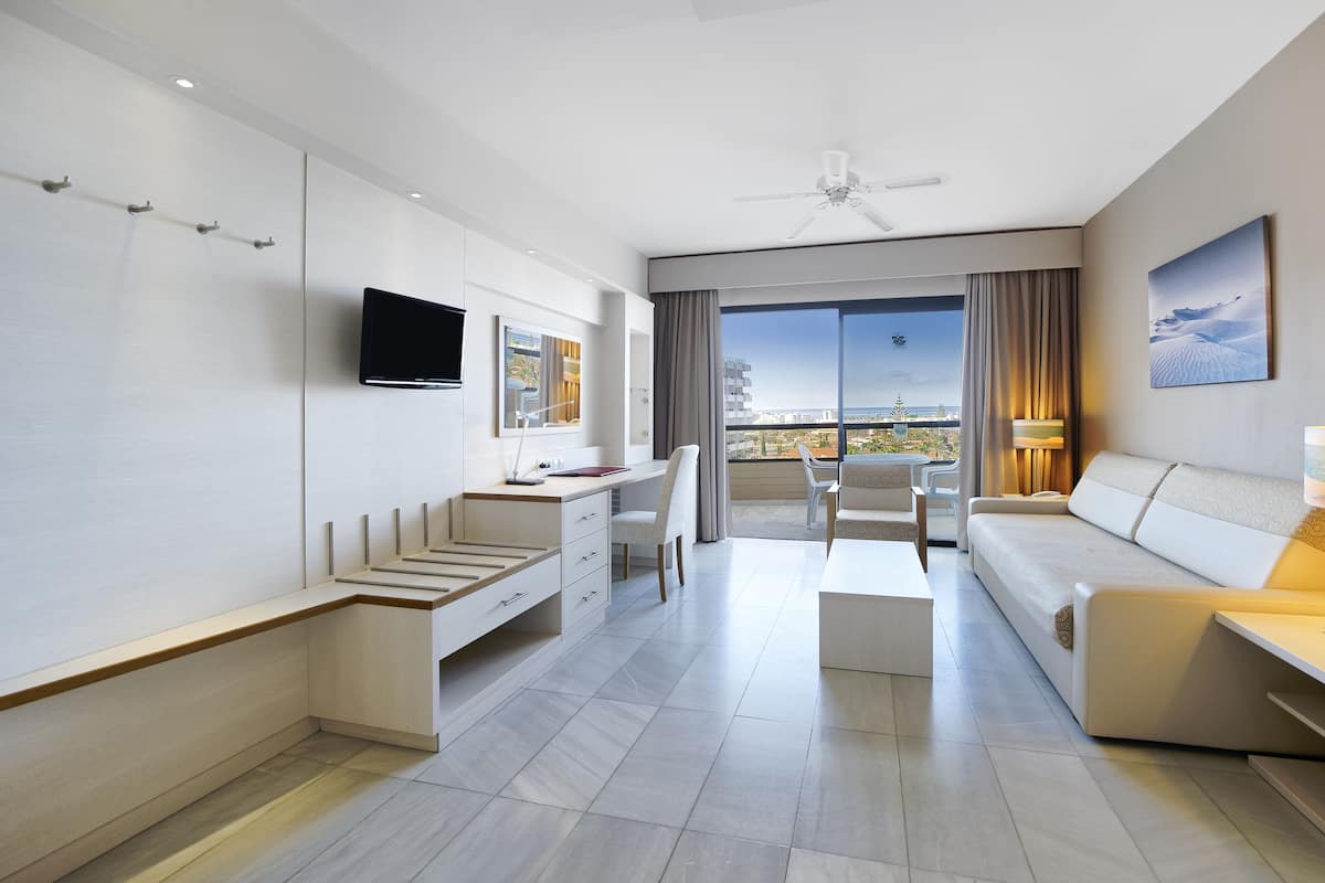 Ein modernes Hotelzimmer mit Balkon, Flachbildfernseher, Schreibtisch, Sofa und Lampe.