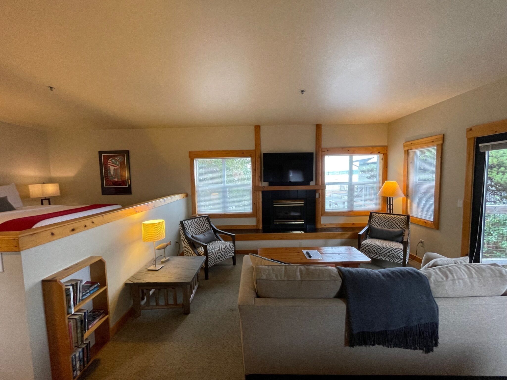 A cozy room with a bed, a sofa, two chairs, a small table, a bookshelf, a fireplace, and a television.