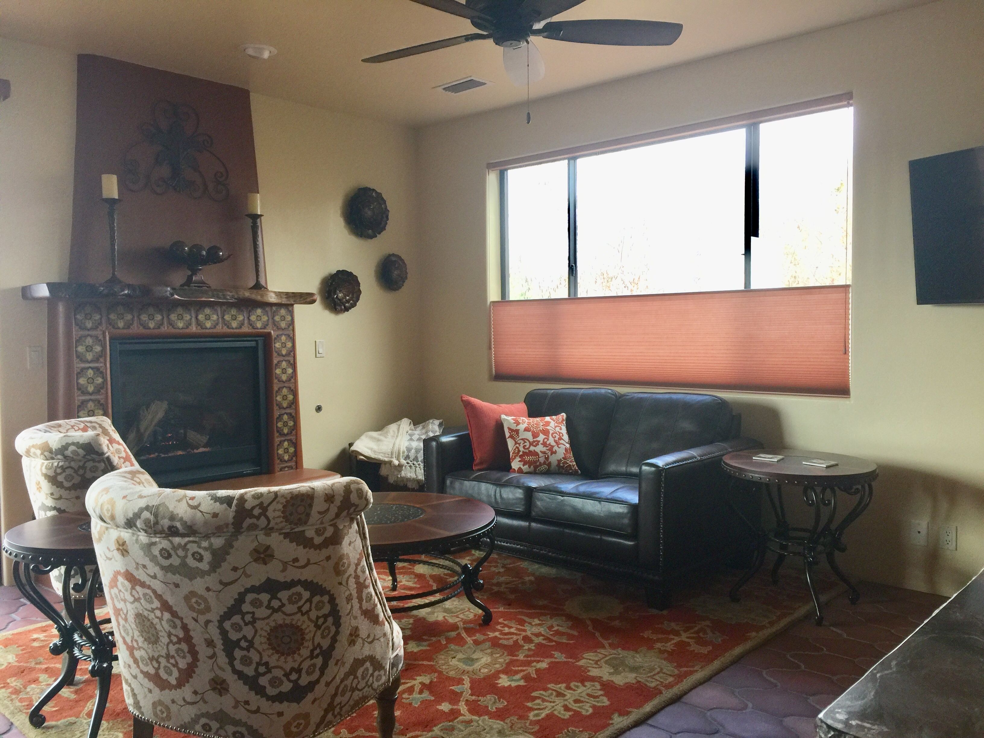 A living room with a fireplace, a sofa, two armchairs, a coffee table, and a large window with blinds.