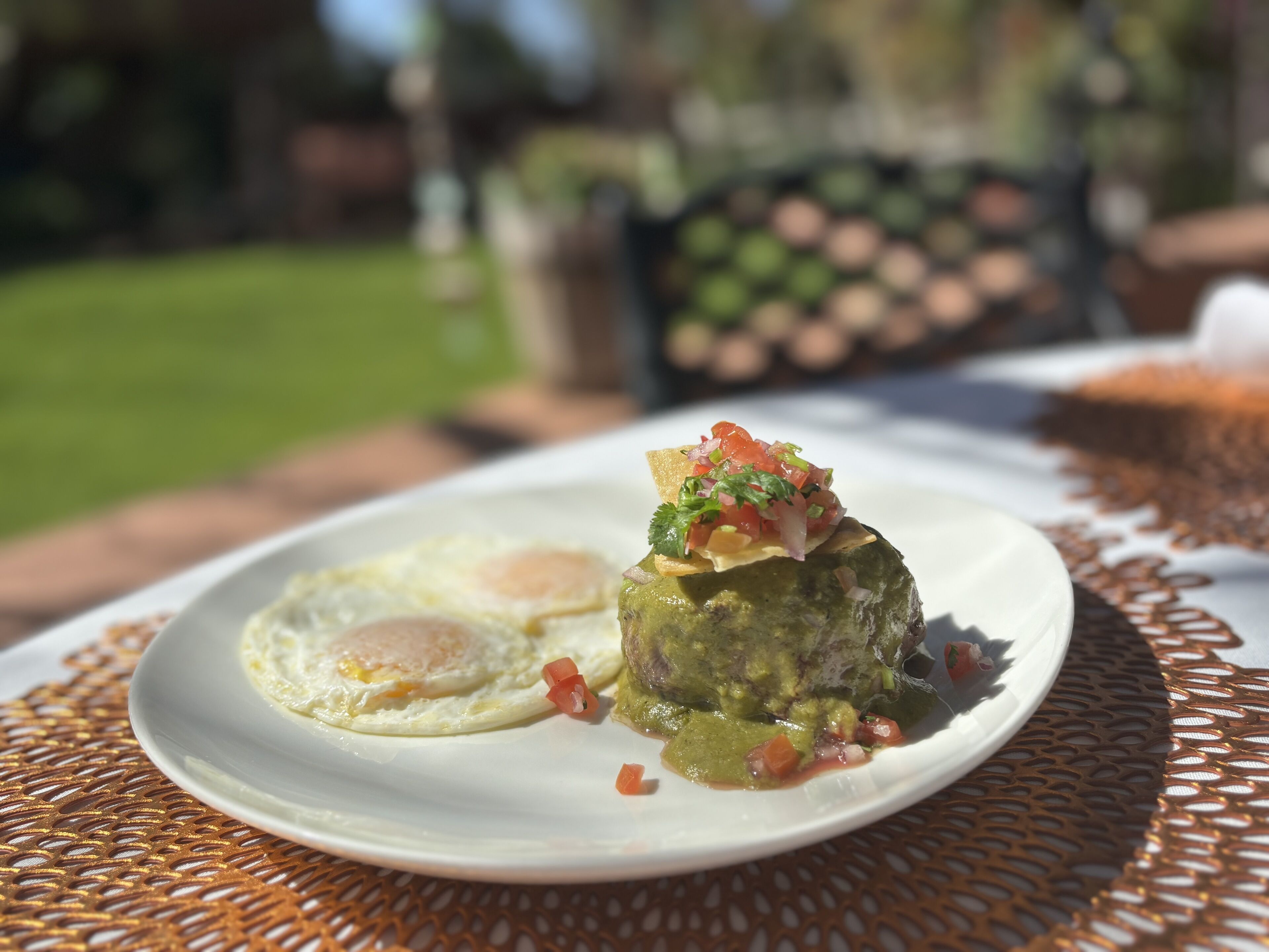 Um prato com um recipiente verde coberto por uma tortilla, um ovo frito e um enfeite de molho de tomate vermelho.