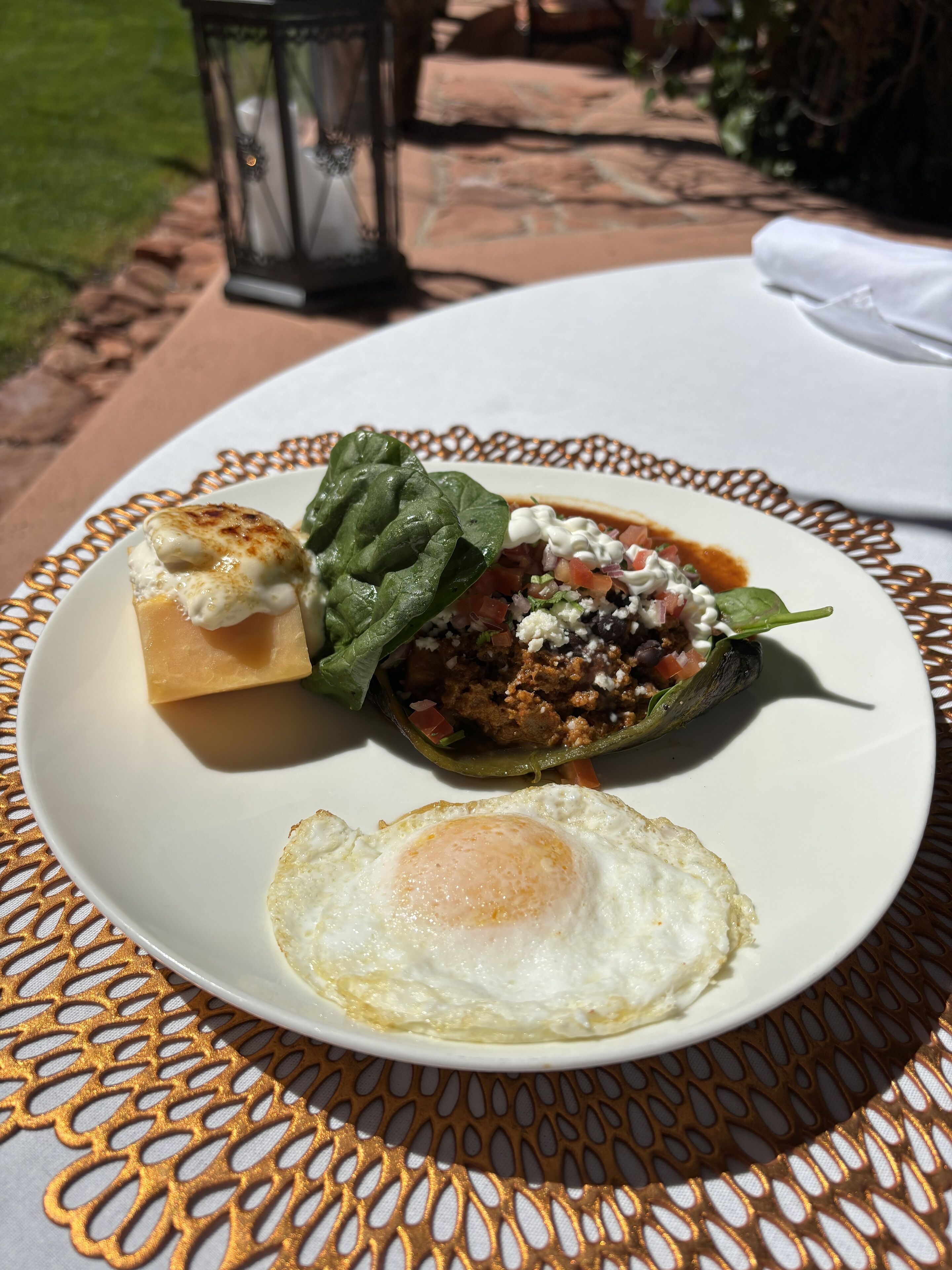 Une assiette contenant un poivron farci, un œuf frit et une tranche de pain, le tout posé sur une nappe à motifs.