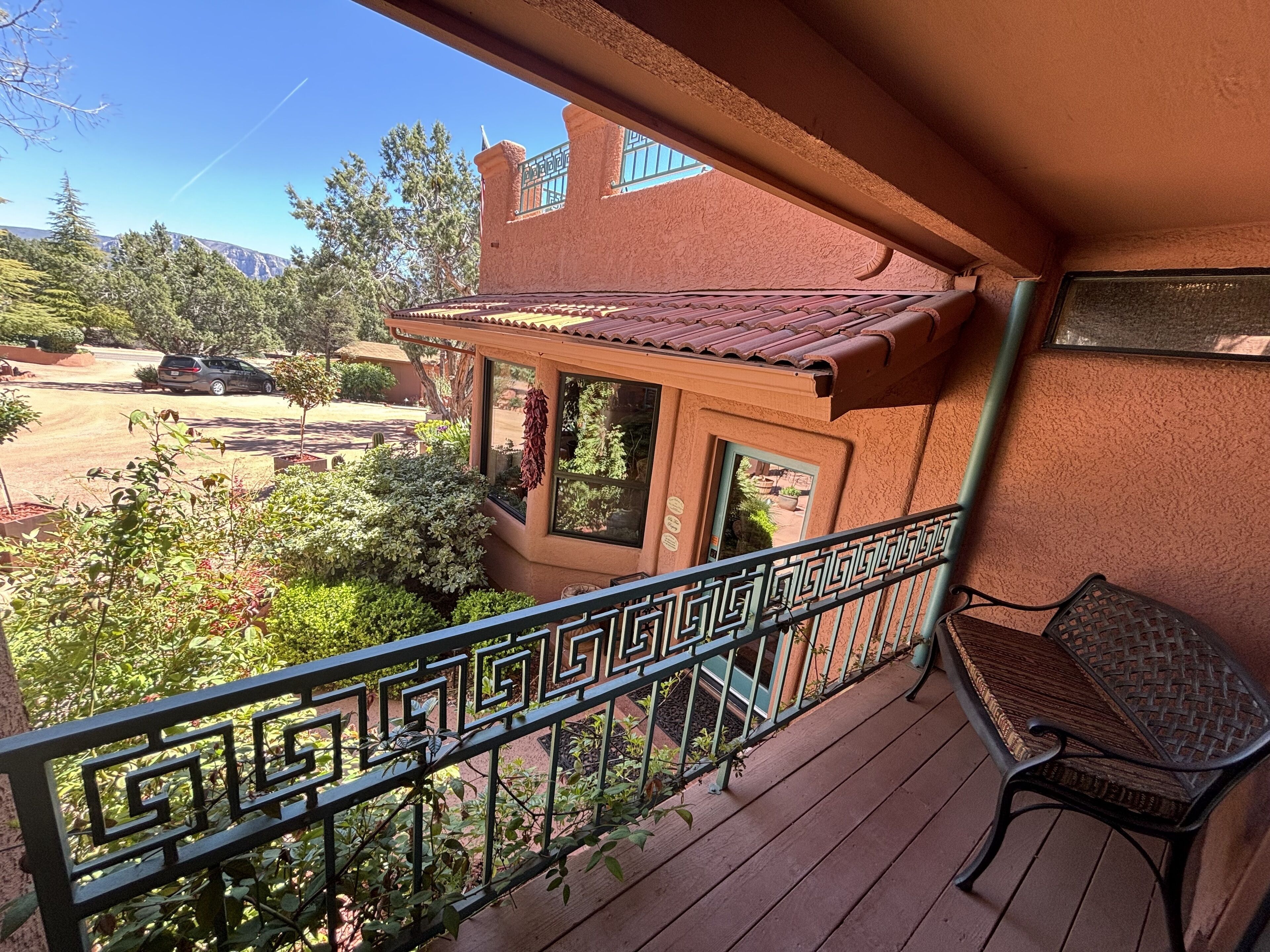 A balcony with a wrought iron railing, a wicker chair, and a view of a red building with a tiled roof.