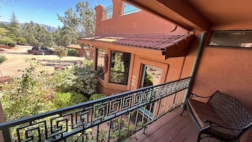 A balcony with a wrought iron railing, a wicker chair, and a view of a red building with a tiled roof.