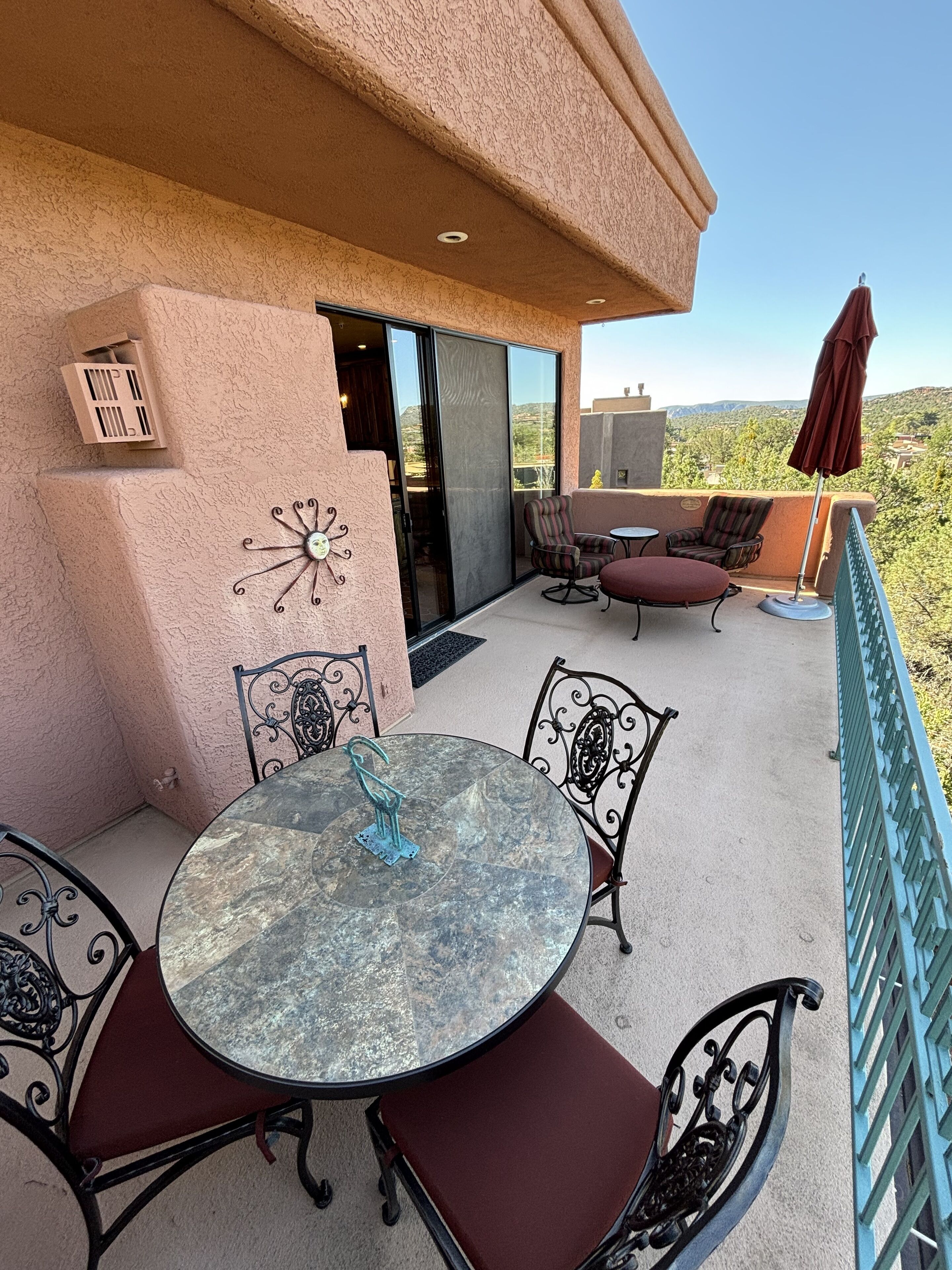 A balcony with a round table and chairs, a decorative wall clock, and a view of the landscape.