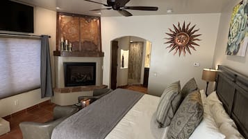 A bedroom with a bed, a ceiling fan, a fireplace, a TV, and a sun decoration on the wall.