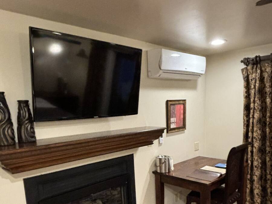 A living room with a flat-screen TV mounted above a fireplace, a table with chairs, and a patterned curtain.