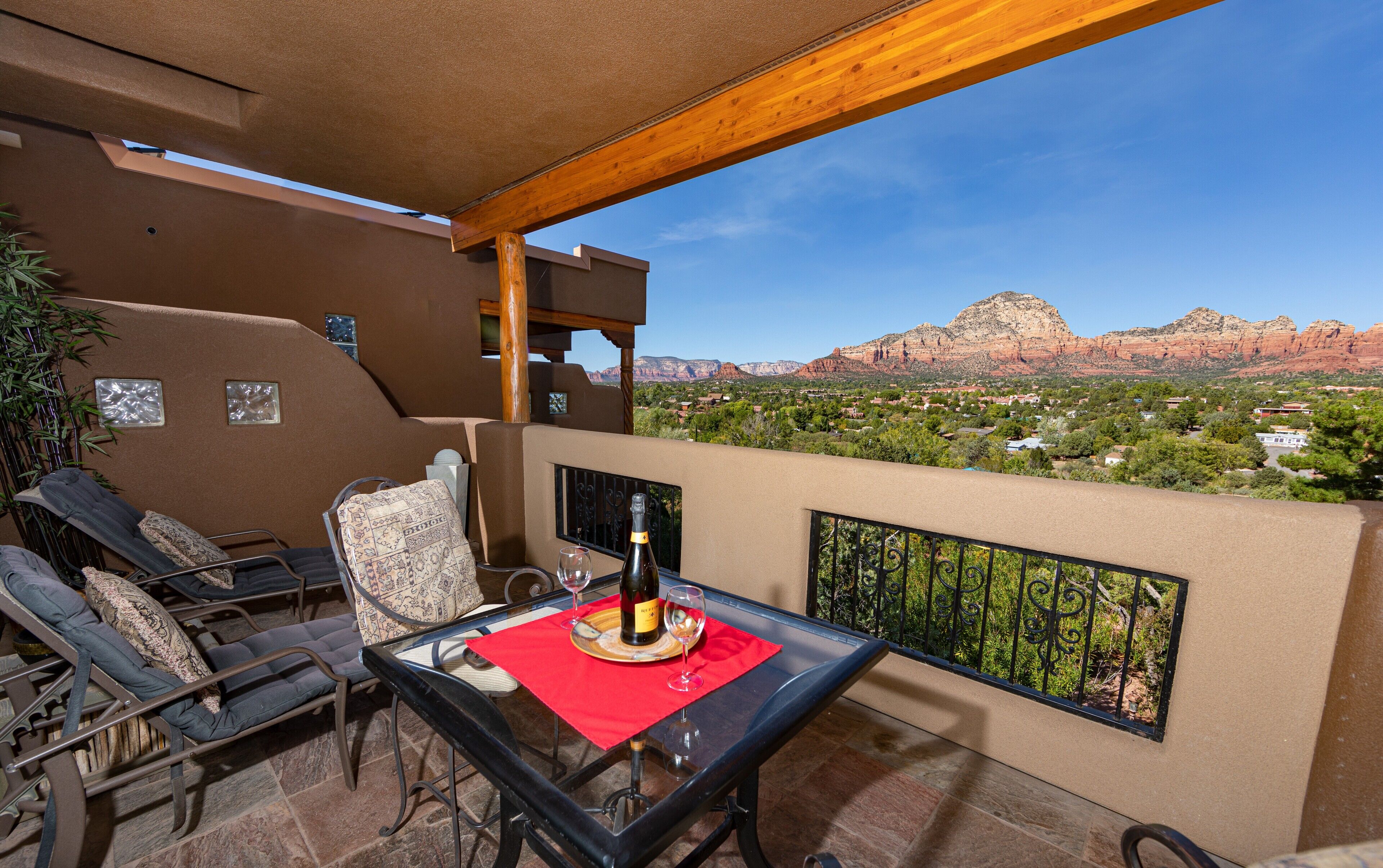 A balcony with a table, chairs, and a bottle of wine. A scenic view of red rock formations and a town is visible in the background.