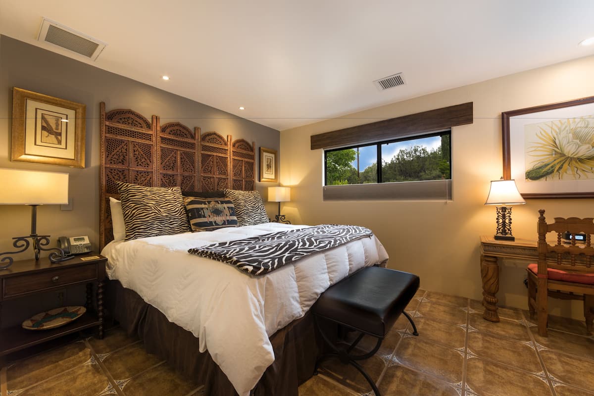 A bedroom with a bed, bedside tables, a bench, a window, and a view of greenery outside.