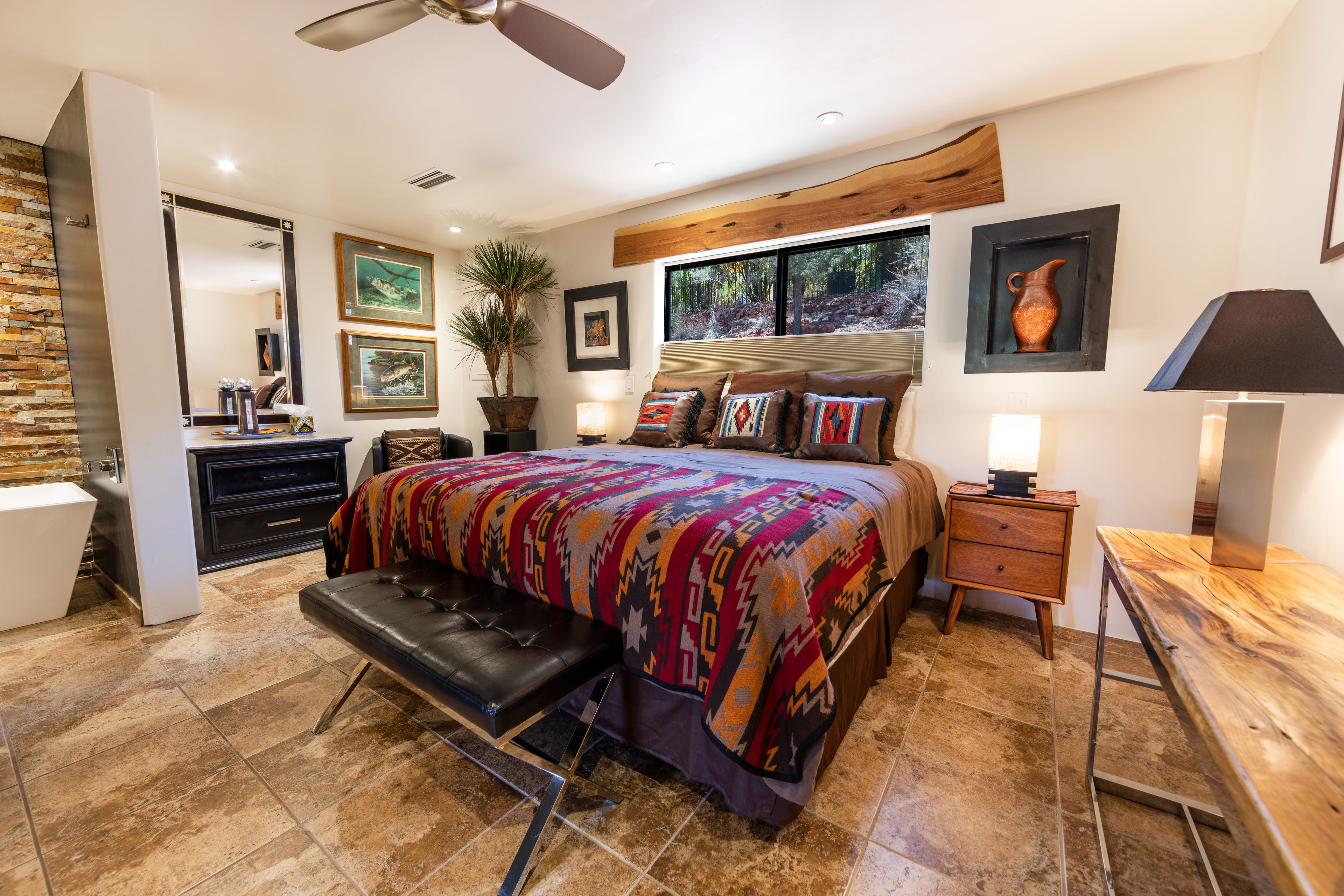 A bedroom with a large bed, a bench, a desk, and a nightstand.