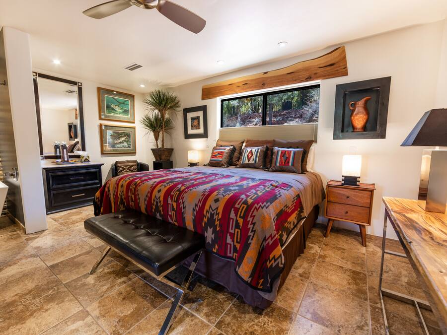 A bedroom with a large bed, a bench, a desk, and a nightstand.