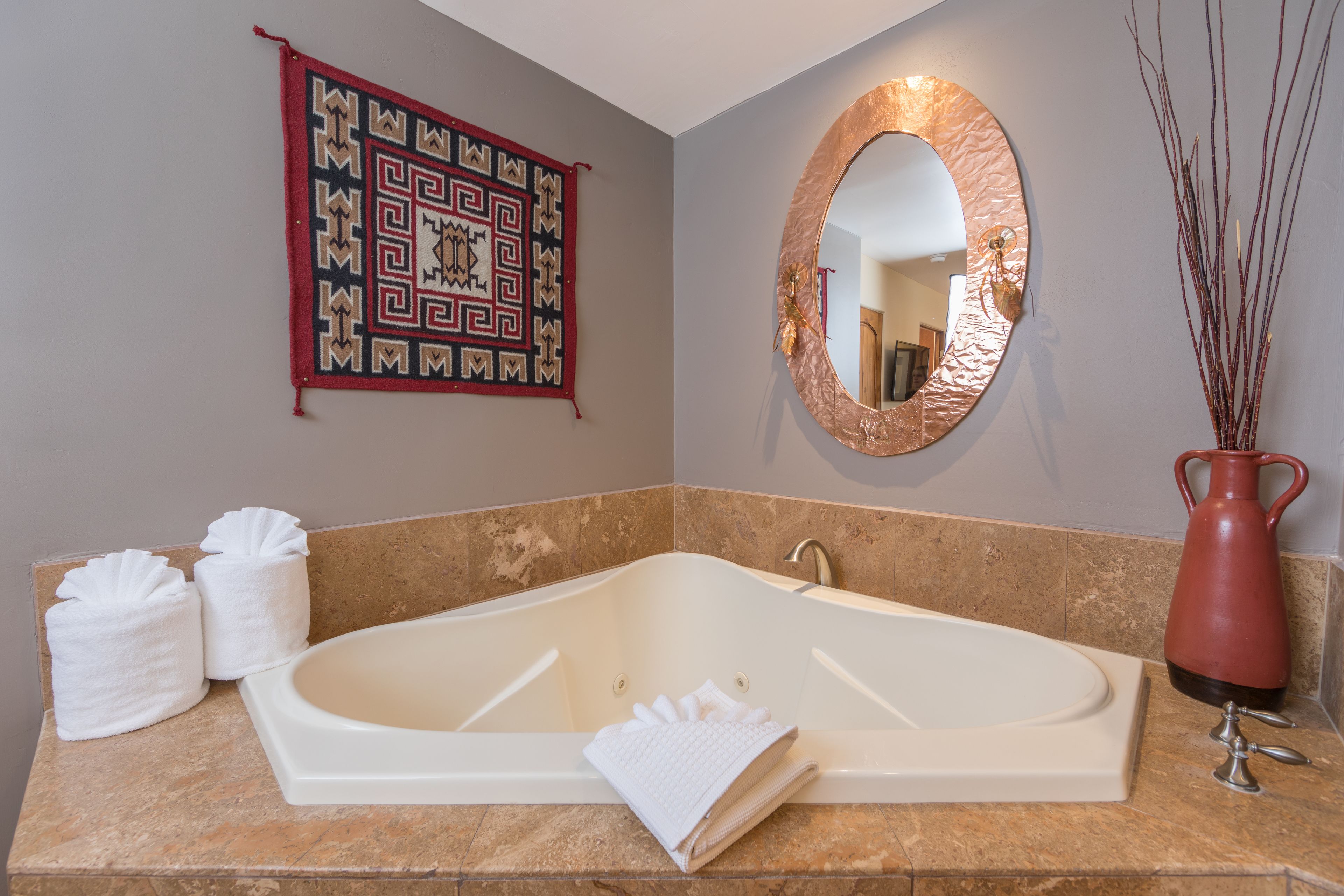 A bathroom with a large bathtub, a mirror, a decorative wall hanging, and two towels on the counter.