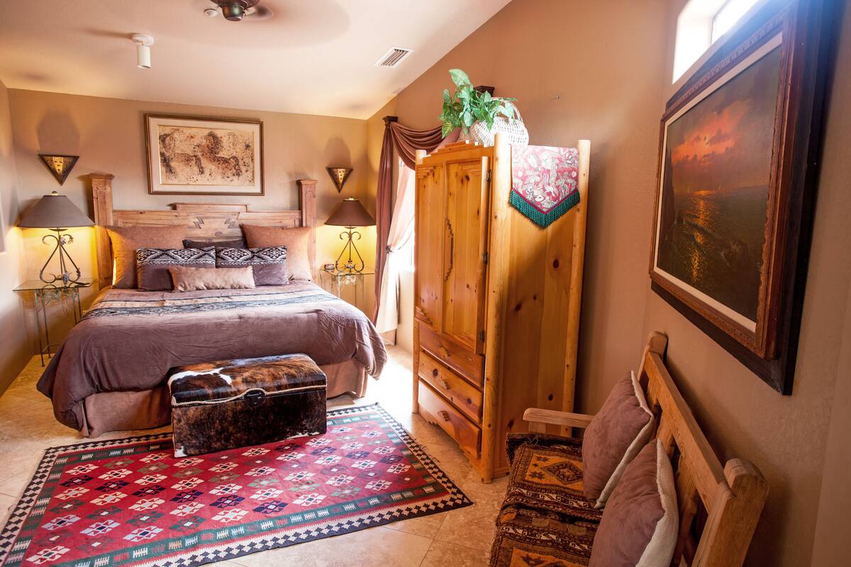A bedroom with a large bed, a wooden wardrobe, a bench, and a rug.