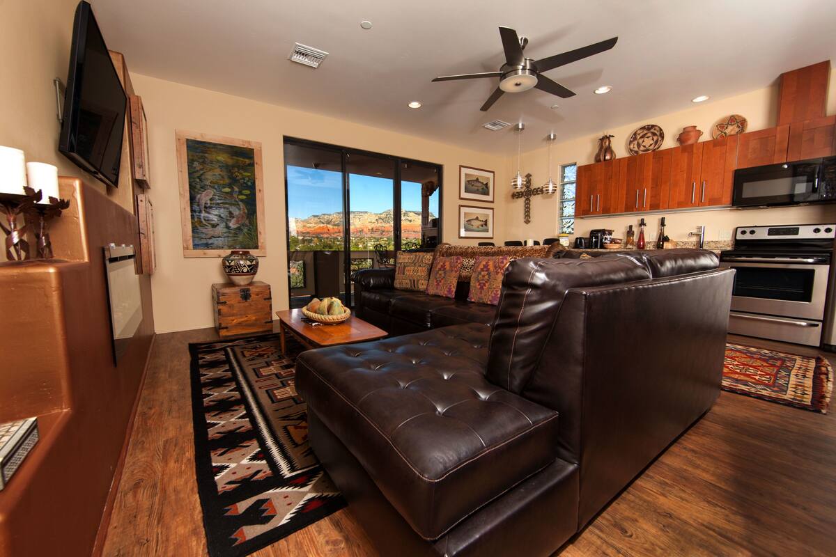 A modern living room with a leather sofa, a flat-screen TV, and a dining area with wooden cabinets and a kitchen with stainless steel appliances.