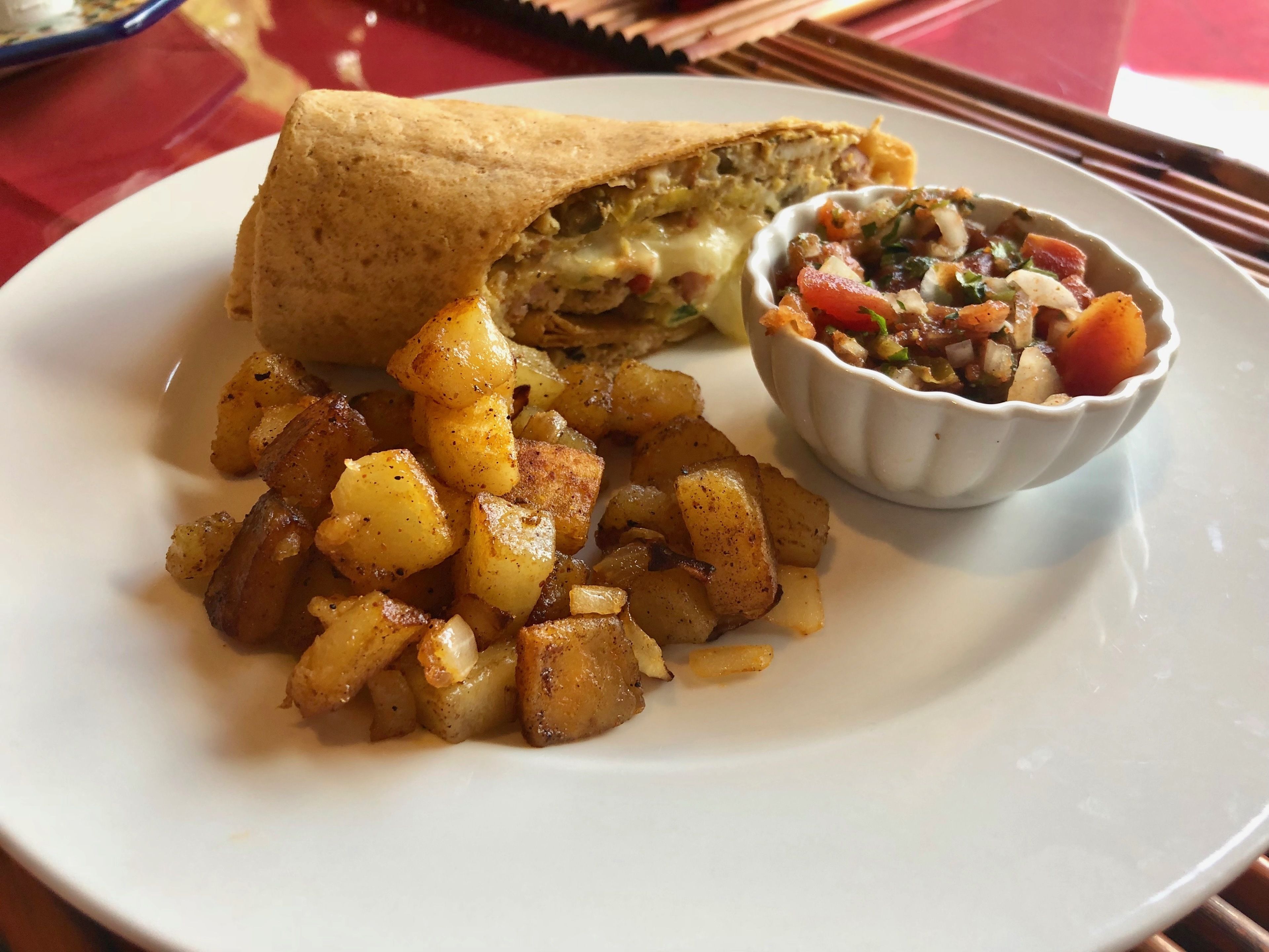 A plate with a wrap, roasted potatoes, and a small bowl of salsa.
